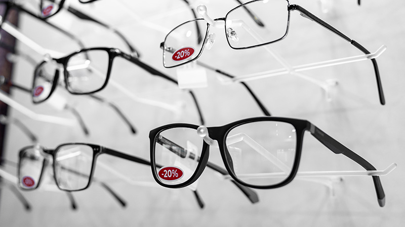 discounted-eyeglass-frames Multiple pairs of black eyeglass frames on a display wall featuring red 20% off sale stickers.