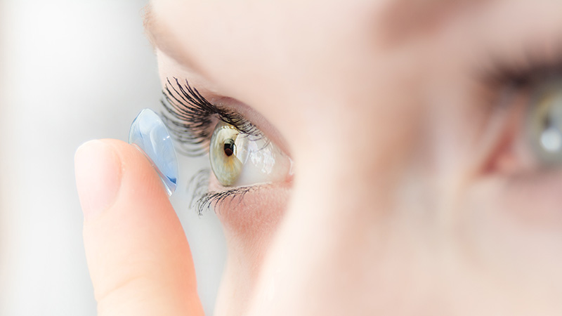 woman-contact-lens-fitting Extreme close-up of a person inserting a clear contact lens onto their eye.